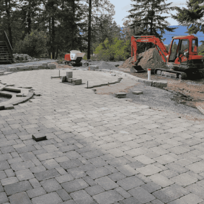 Landscape installation in progress featuring paving stones, retaining walls, stairs, and lush planting on a residential property in the Okanagan.