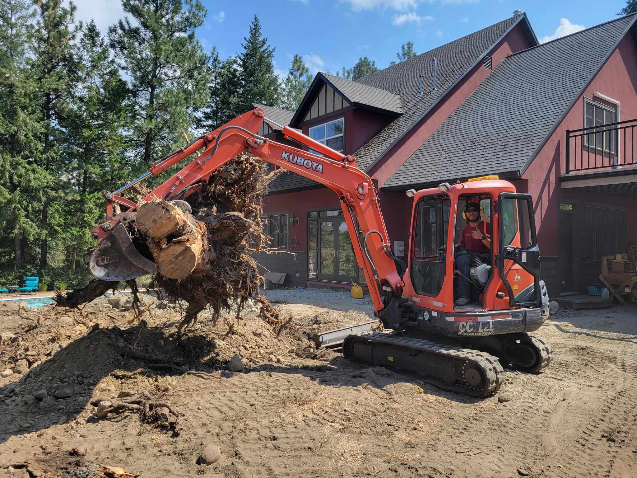 Excavator removing a large tree stump during landscape construction site preparation in Kelowna, BC